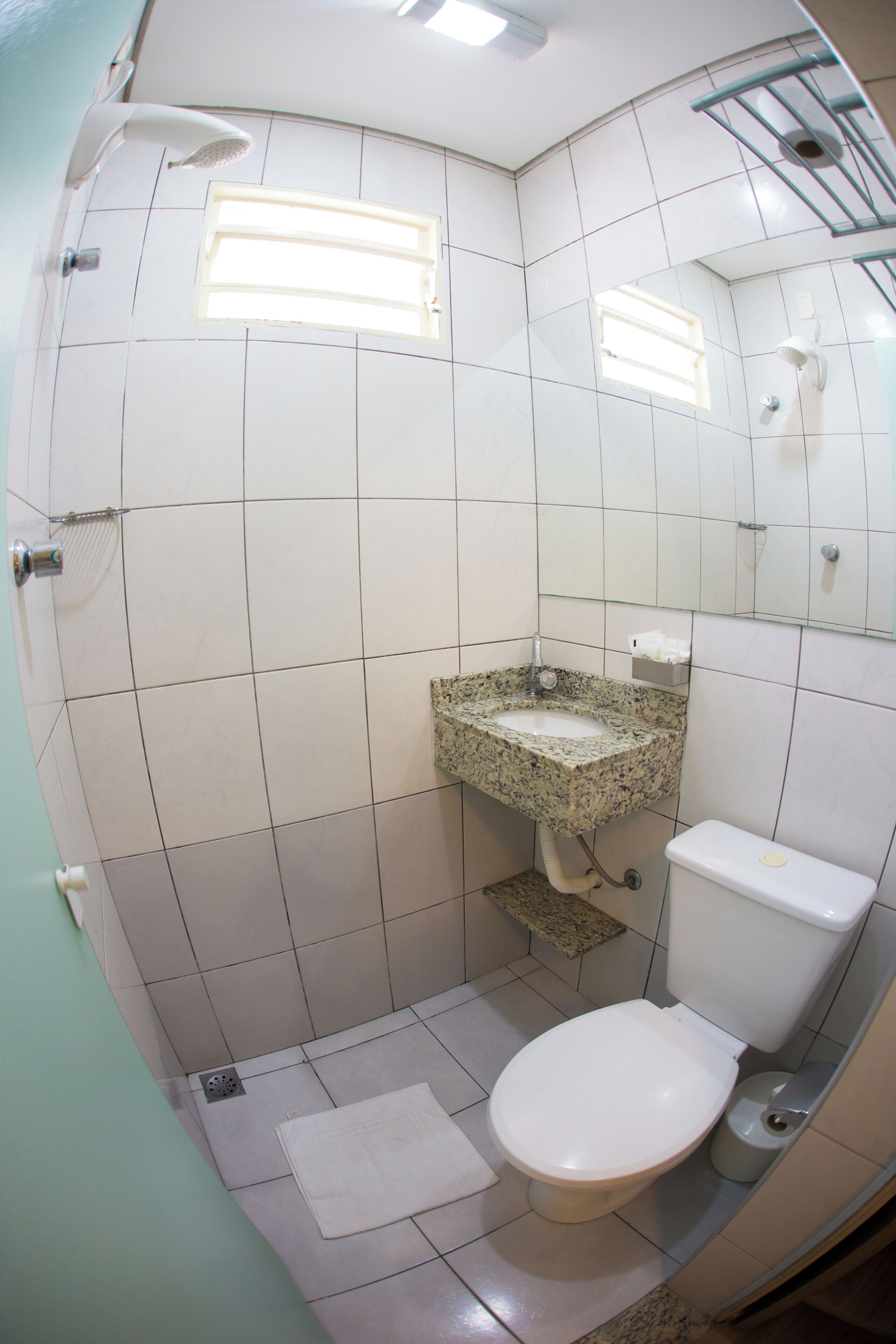 Un baño con inodoro blanco, lavabo de granito, ducha y una ventana pequeña.