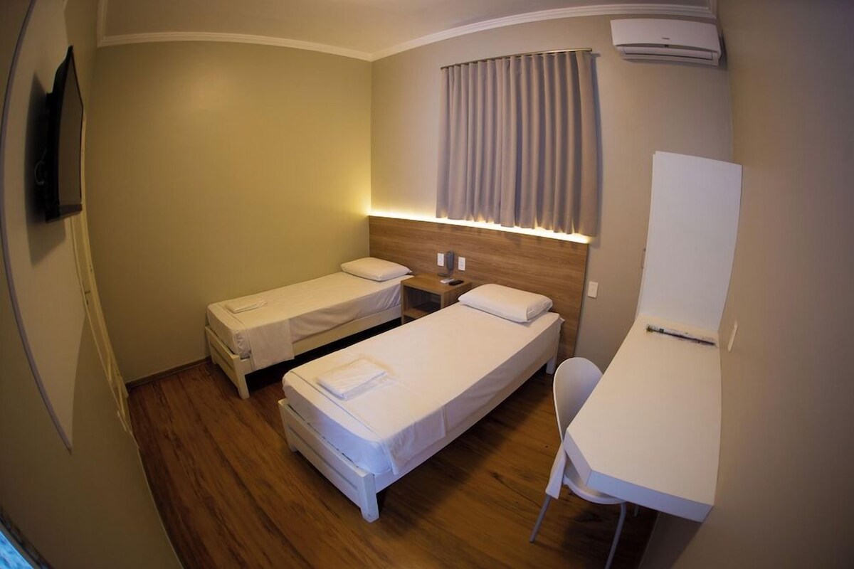 Habitación de hotel con dos camas individuales, un escritorio, una silla, un televisor de pantalla plana y un equipo de aire acondicionado.