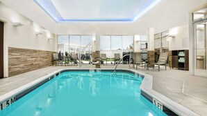 Une piscine intérieure à l’eau claire, entourée de chaises longues et offrant une vue sur un bâtiment blanc.