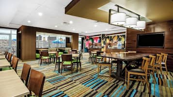 A modern dining area with striped carpet, wooden tables and chairs, and a large TV screen.