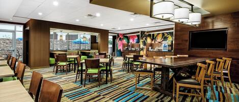 A modern dining area with striped carpet, wooden tables and chairs, and a large TV screen.