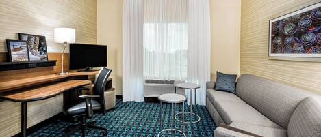 Habitación de hotel con escritorio, silla, televisión, sofá y alfombra estampada.