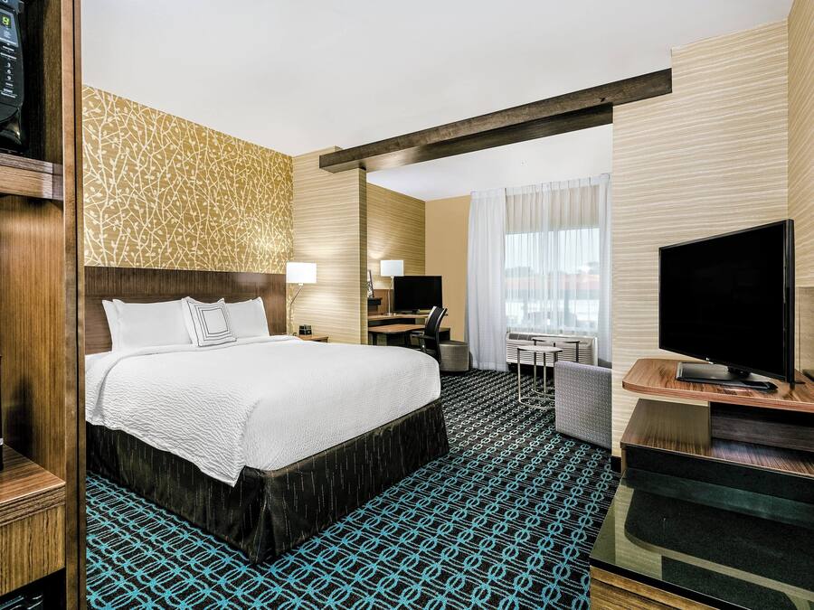 Quarto de hotel com cama, escrivaninha, televisão e minibar.
