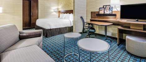 Una habitación de hotel con cama, escritorio, televisor, sofá y alfombra estampada.