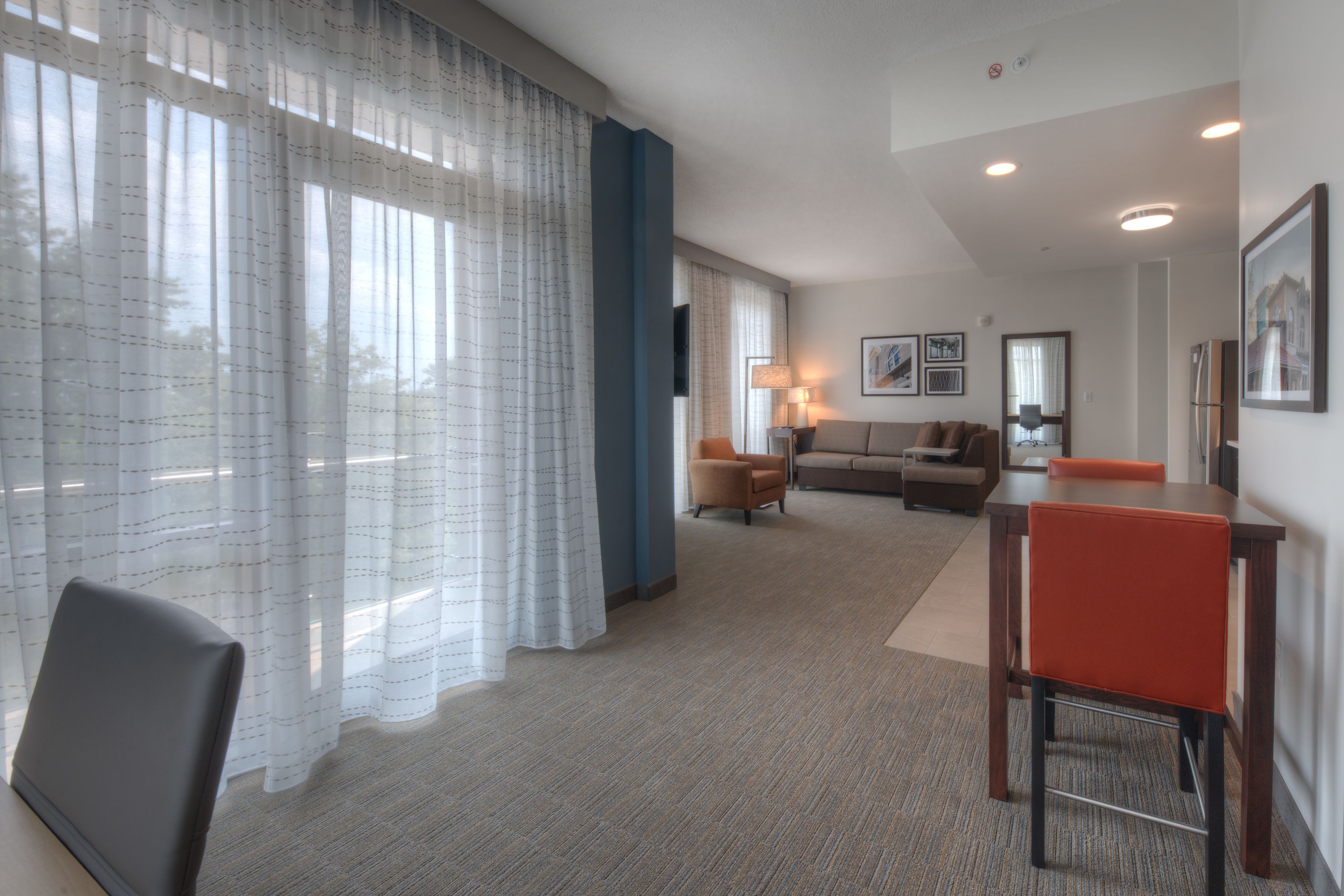 A hotel room with a large window, a sofa, a dining table, and a chair.