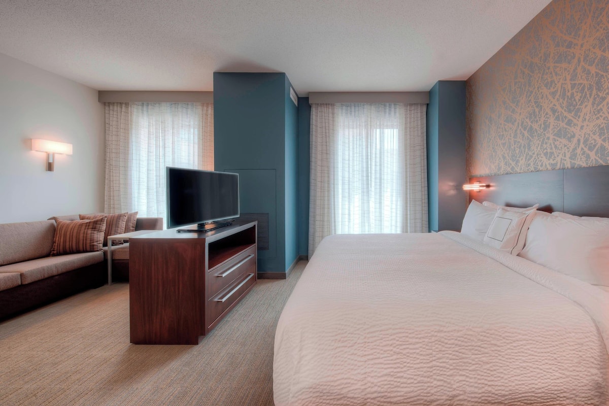 Una camera d'albergo con un letto grande, una TV su un supporto in legno, un divano e una scrivania.