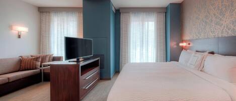 A hotel room with a large bed, a TV on a wooden stand, a sofa, and a desk.