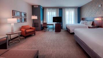 A hotel room with a bed, a desk, a chair, a TV, and a lamp.