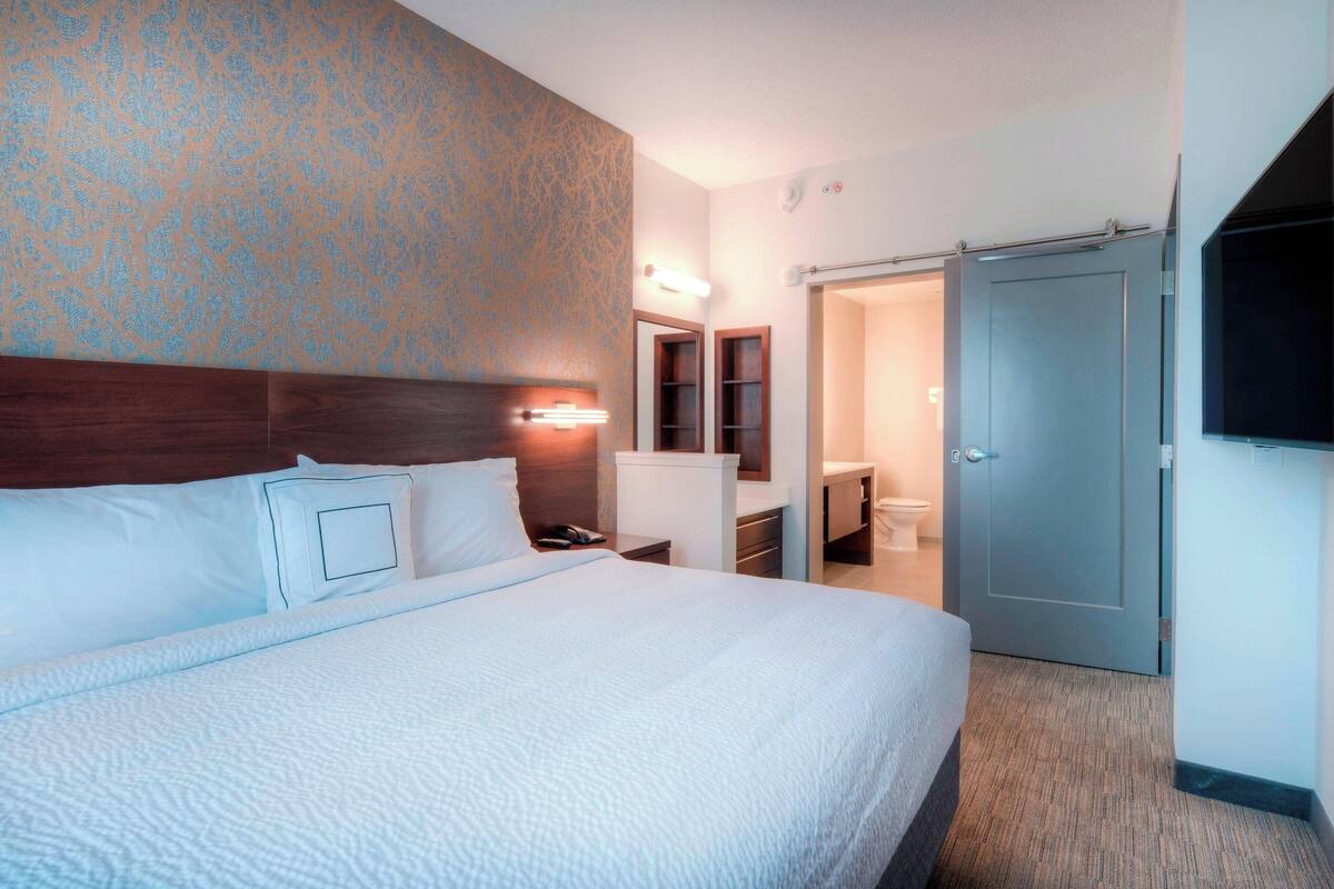 Camera d'albergo con un letto grande, una testiera in legno, un bagno con il water e un lavandino, e una porta chiusa.