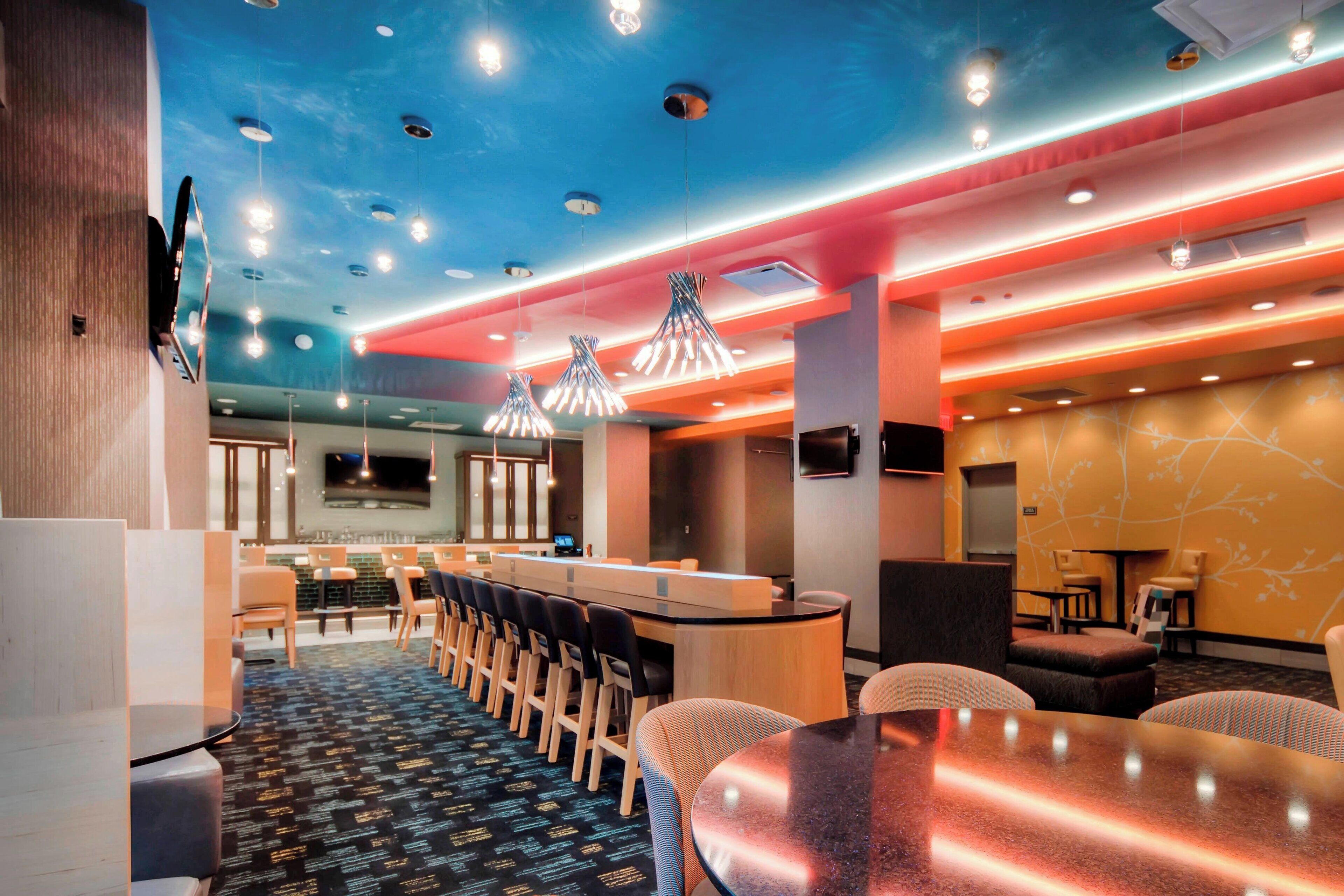 Un hall d’hôtel moderne avec un long comptoir d’accueil, plusieurs espaces aménagés pour s’asseoir et une moquette à motifs.