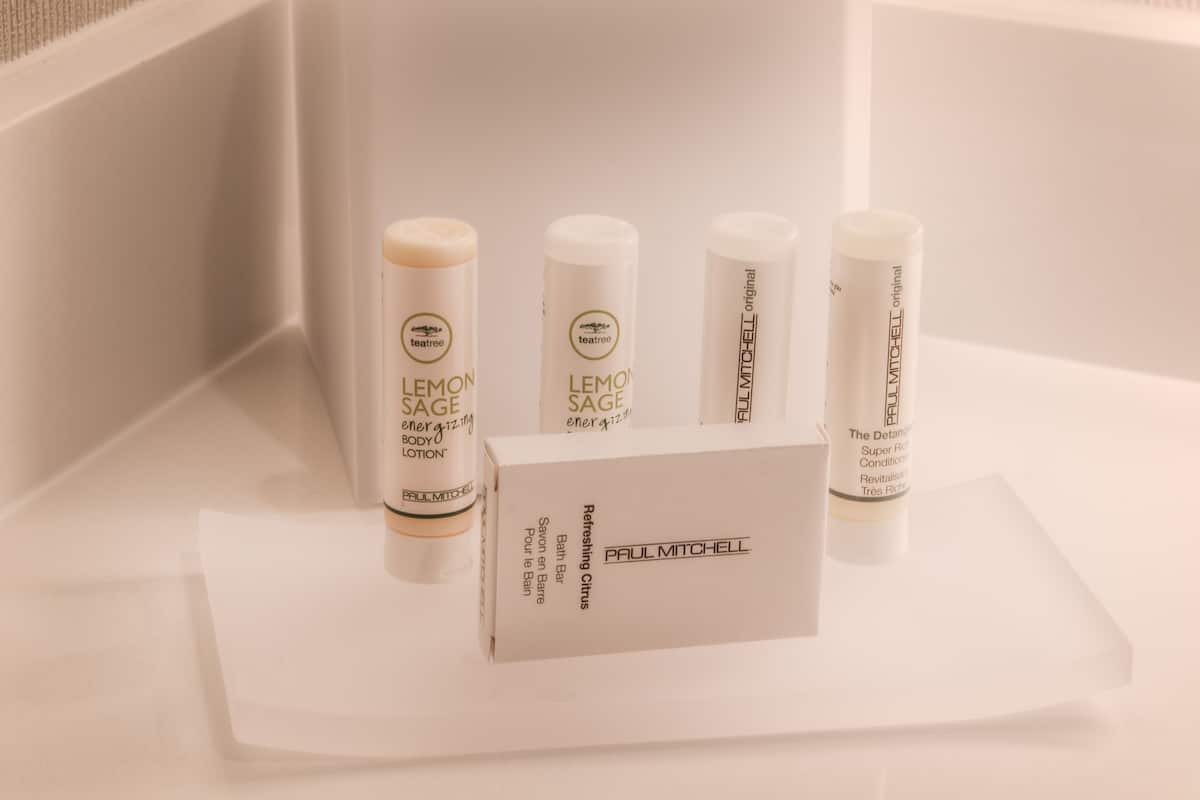 Un bagno con una scatola di fazzoletti bianchi, quattro flaconi di lozione corpo Paul Mitchell Lemon Sage e una saponetta da bagno bianca.