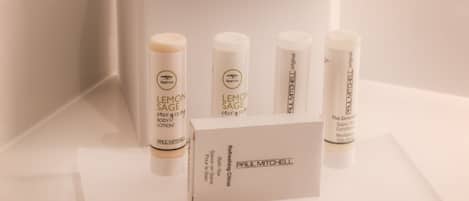 A bathroom with a white tissue box, four bottles of Paul Mitchell Lemon Sage body lotion, and a white bath bar.