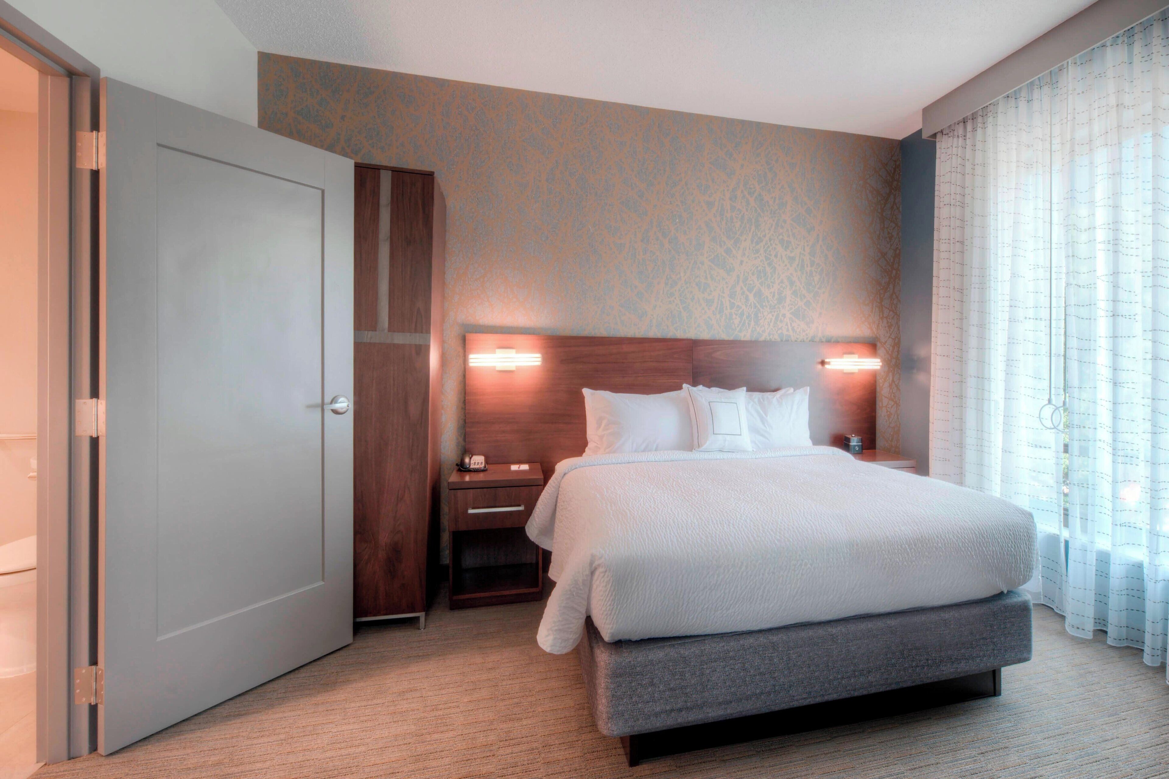 A hotel room with a large bed, a nightstand, a wooden wardrobe, and a door.