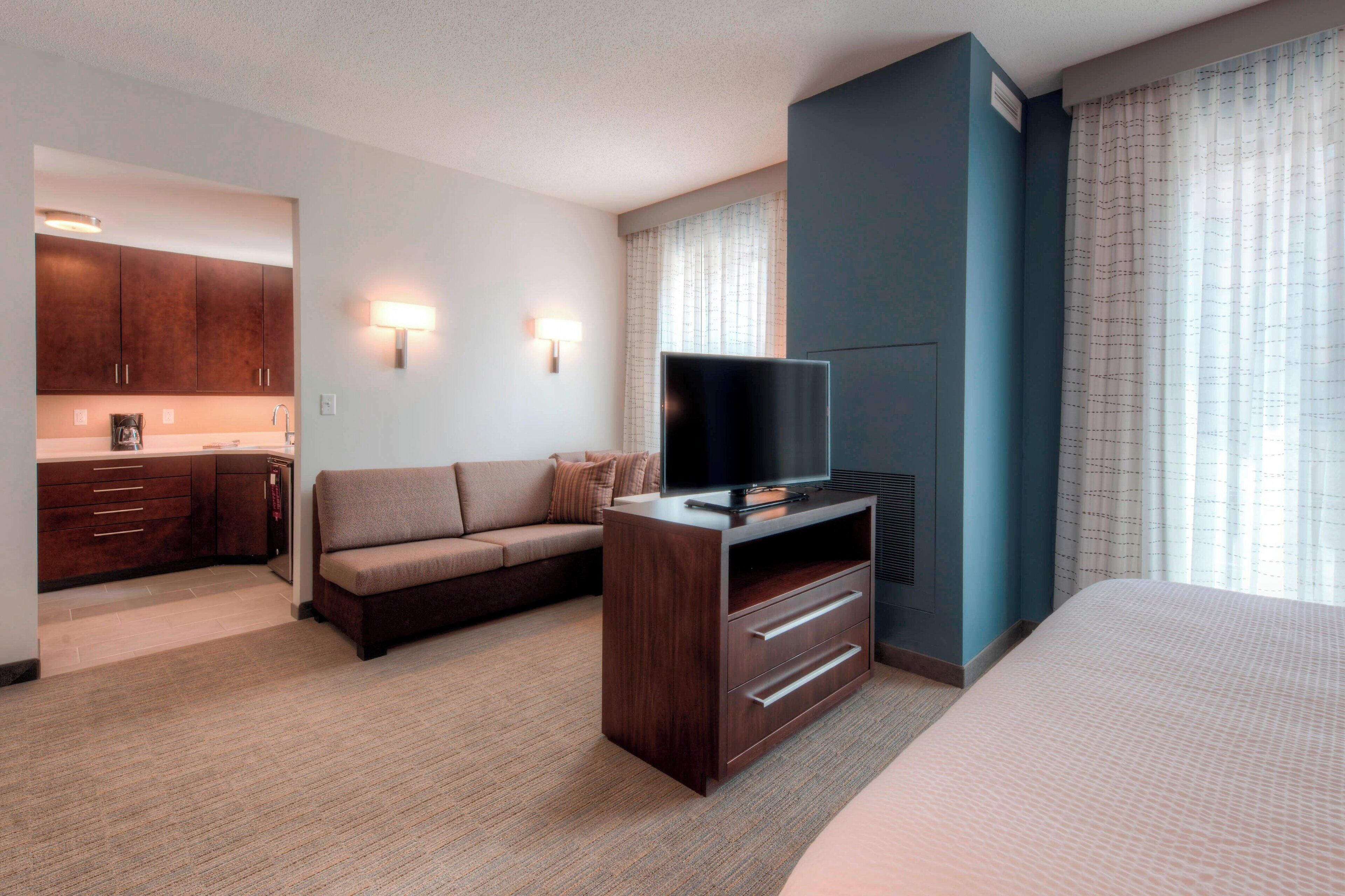 Ein Hotelzimmer mit Bett, Fernseher auf einem Holzständer, einer Couch, einer Küchenzeile und einem Badezimmer.