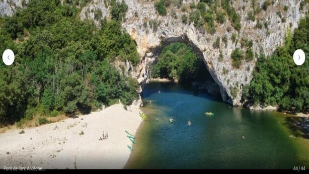 Un arco de roca natural sobre una playa con kayak y un cielo azul despejado.