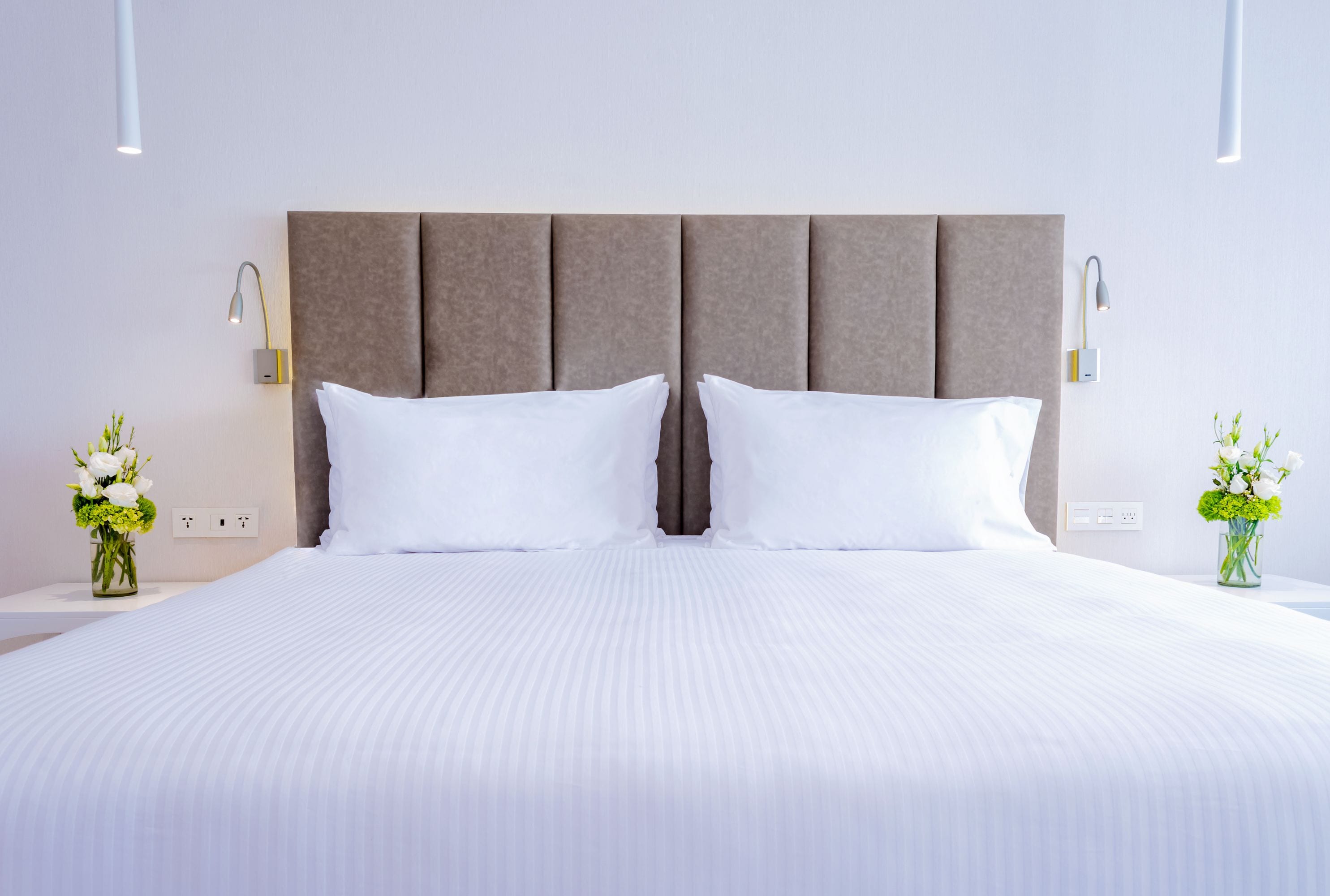 A neatly made bed with a padded headboard, two bedside tables with lamps, and a vase of flowers on each side.