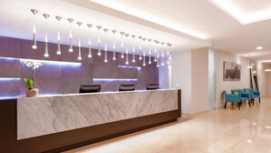A modern reception desk with a marble top, multiple pendant lights, and a vase of flowers. There are three chairs and a painting on the wall. - NH Puebla Finsa (Puebla)