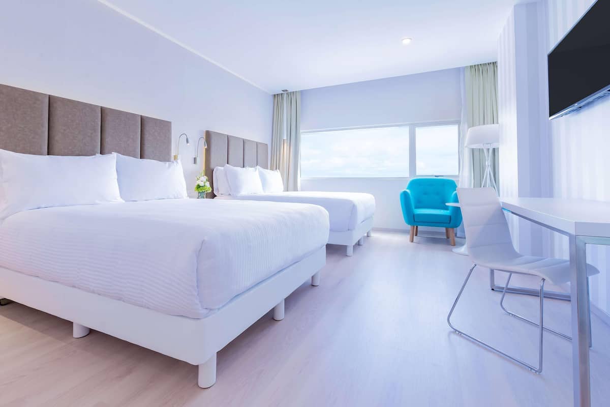 A modern hotel room with two beds, a desk, a chair, and a large window.