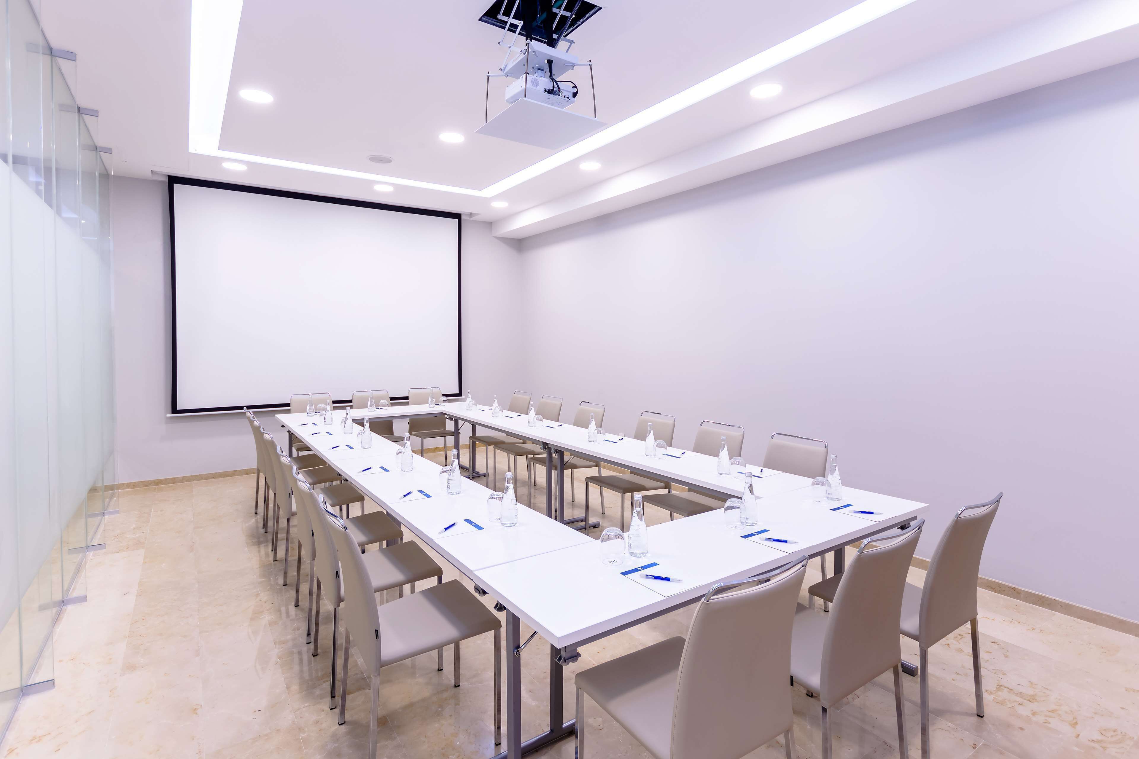 Una sala de conferencias con una mesa larga, sillas, una pantalla de proyector y una pizarra.