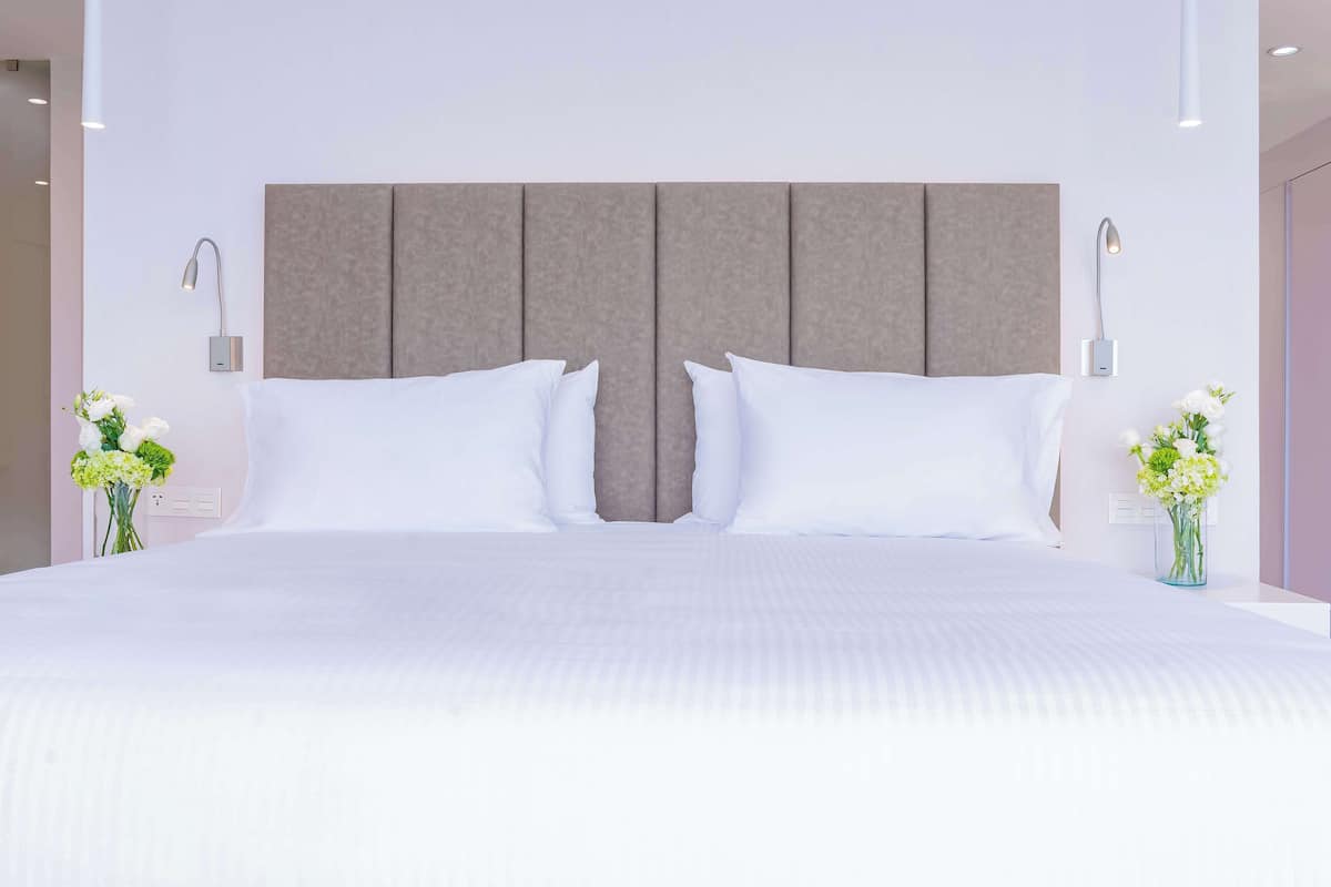 A modern hotel room with a large bed, two bedside tables, and a neutral-toned headboard.