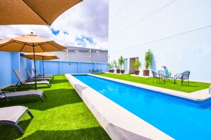 A swimming pool with sun loungers and umbrellas, surrounded by a blue wall and potted plants. - NH Puebla Finsa (Puebla)