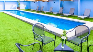 A swimming pool with lounge chairs and umbrellas, surrounded by artificial grass and a blue wall. - NH Puebla Finsa (Puebla)