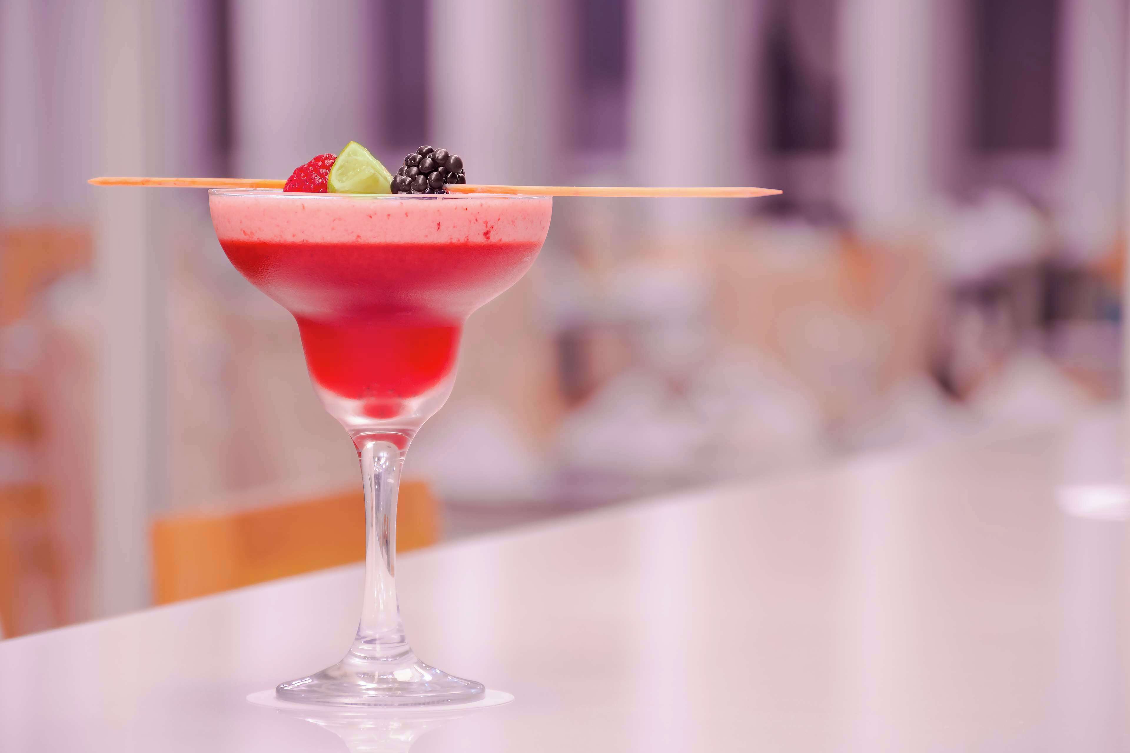 Un cocktail servi dans un verre à martini, garni d’une tranche de citron vert et de quelques fruits rouges sur le bord du verre.