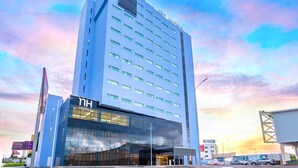 A modern hotel with a glass facade, multiple floors, and a prominent entrance. - NH Puebla Finsa (Puebla)