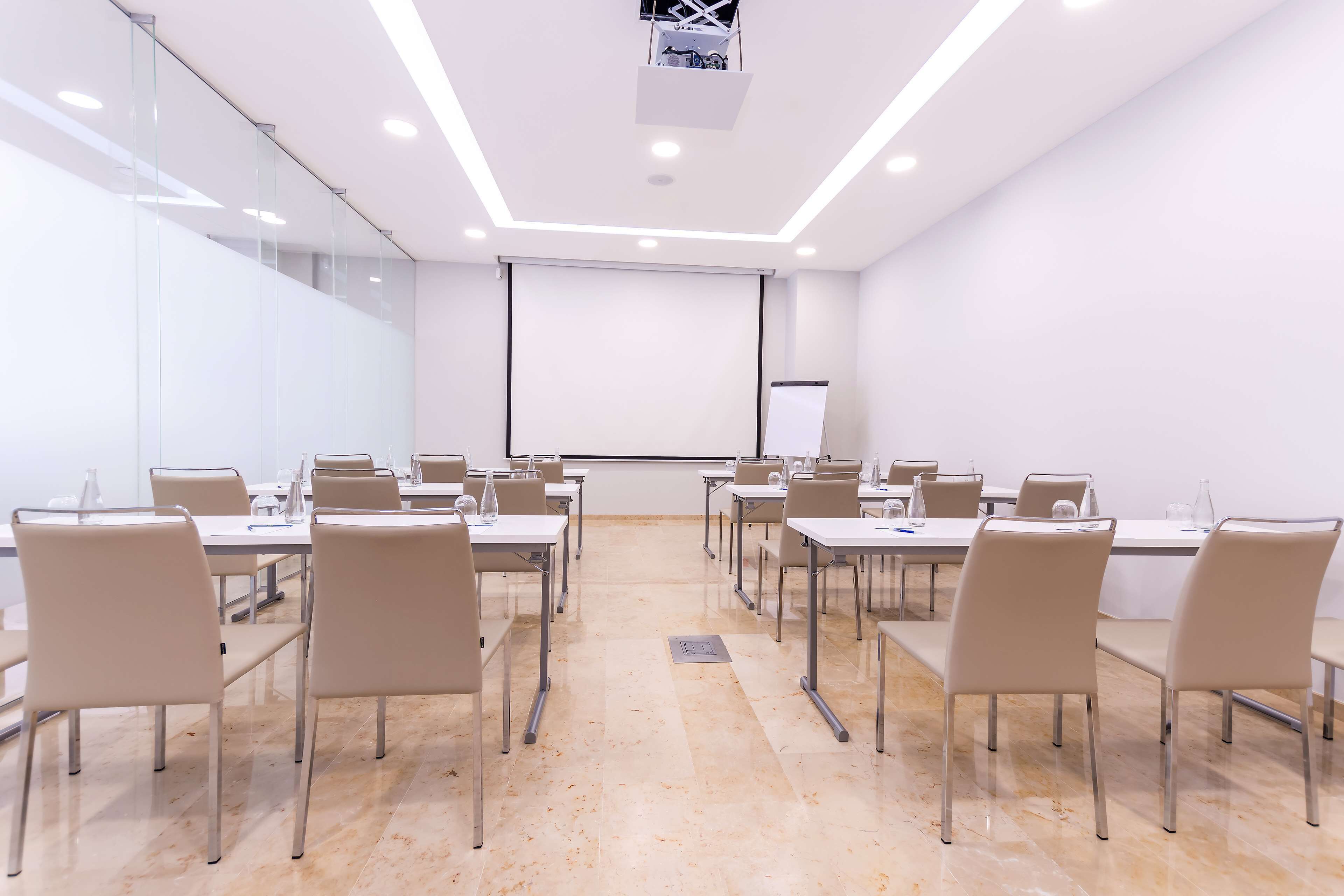 A conference room with a projector screen, white walls, and a marble floor.