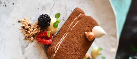 Un postre en un plato con cacao en polvo, frambuesas, moras y hojas de menta.
