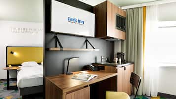 A hotel room with a bed, a desk with a chair, a small kitchenette, and a television displaying the Park Inn logo.