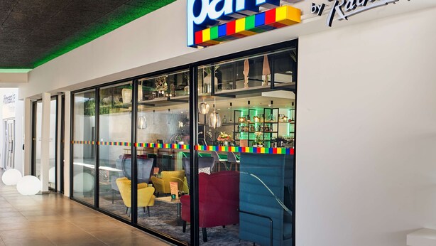 A Park Inn hotel with a modern design, featuring a large illuminated sign, glass walls, and a variety of seating options inside. - Park Inn by Radisson Hasselt (Hasselt)