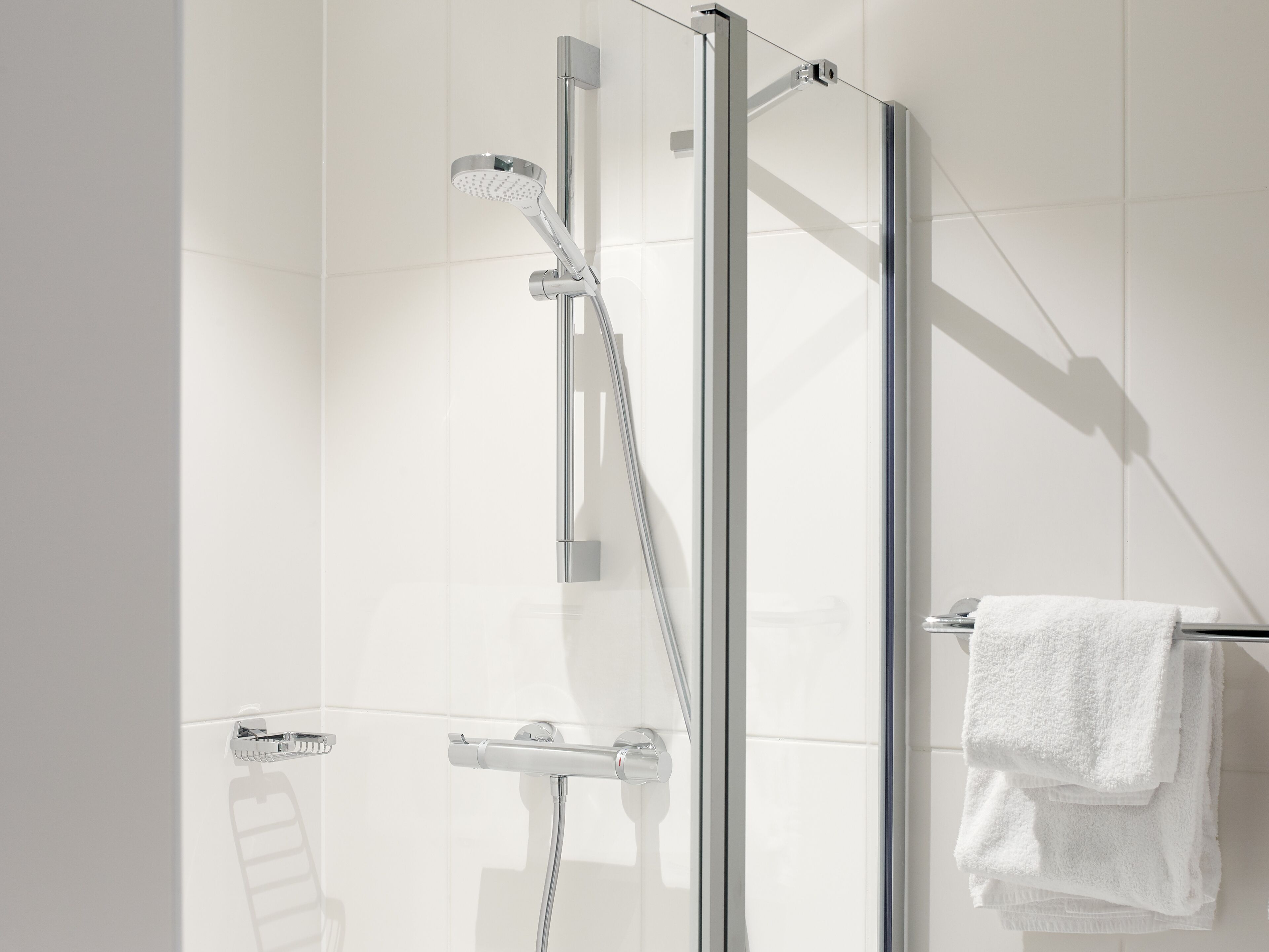 A modern bathroom with a glass shower enclosure, chrome fixtures, and a towel rack with folded towels.