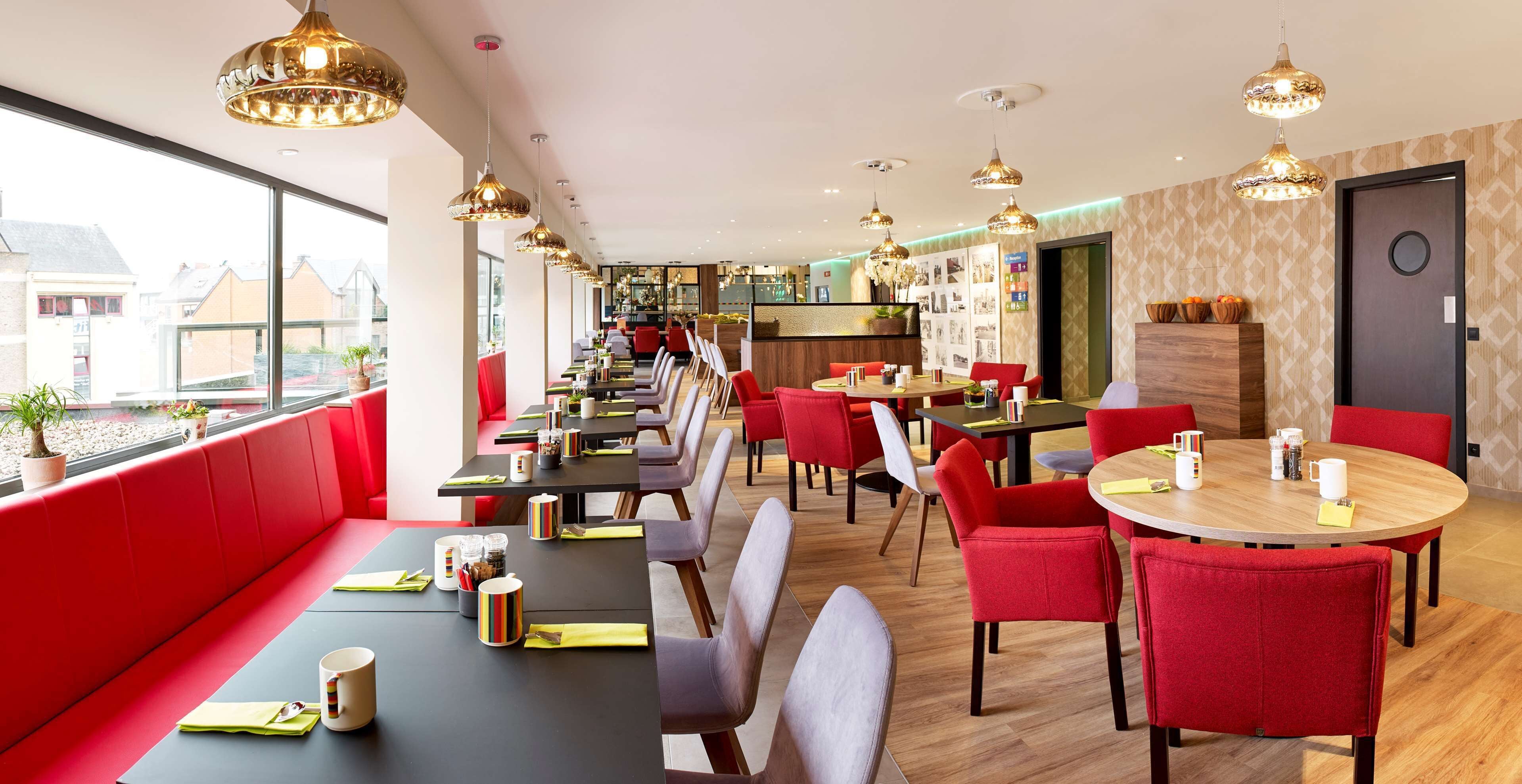 A modern restaurant with red seating, multiple dining areas, and pendant lighting.
