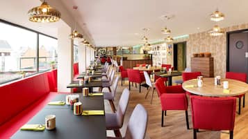 A modern restaurant with red seating, multiple dining areas, and pendant lighting.