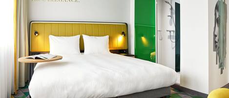 Habitación de hotel con una cama grande, una mesita de noche, una puerta verde y una pared con una cita sobre la sencillez.