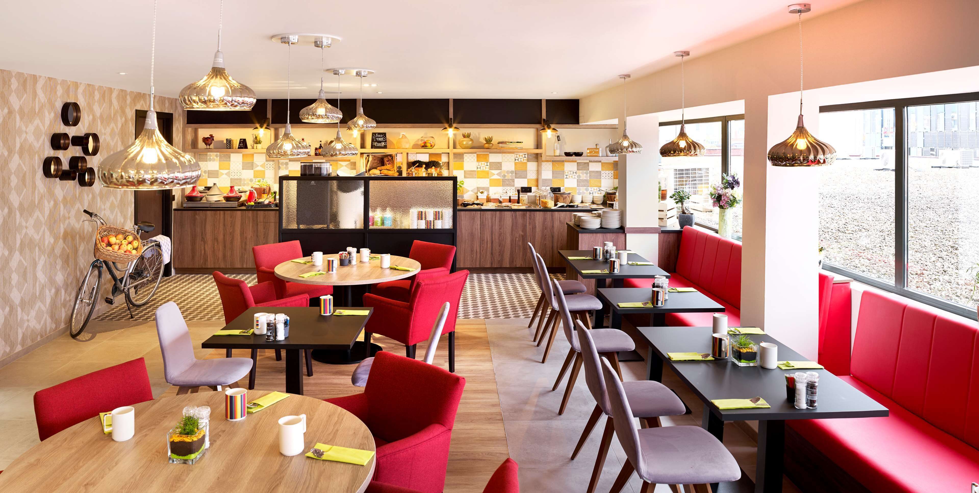 A modern restaurant with round tables, red and grey chairs, and pendant lighting.