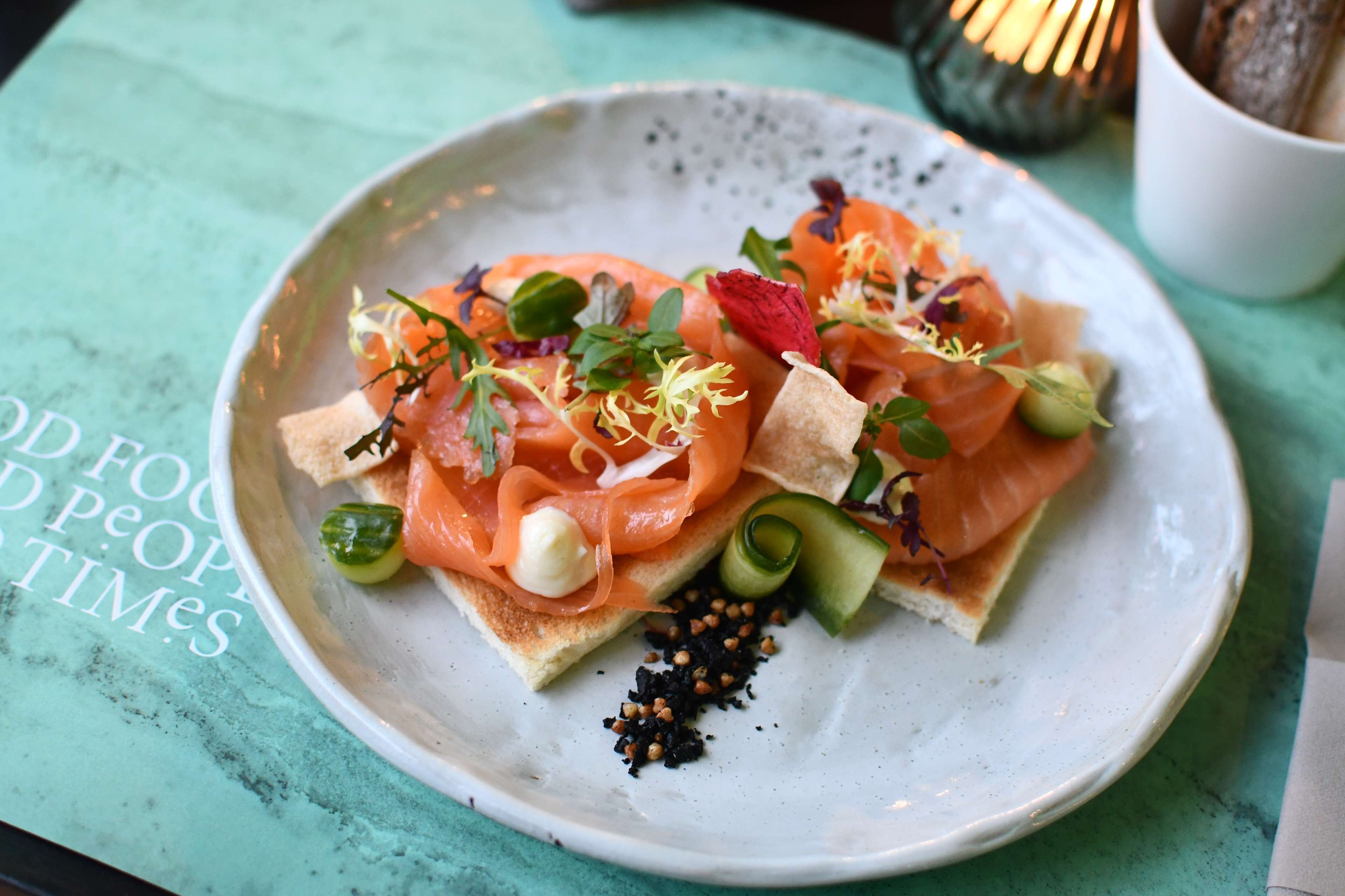 A plate of food with smoked salmon, avocado, and garnishes on a ceramic plate.