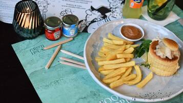 Um prato com batatas fritas e um hambúrguer, uma lata de ketchup Heinz, uma garrafa de Fanta e um menu verde com ilustrações de comida.
