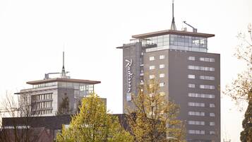 A modern building with a prominent antenna on top, surrounded by trees.