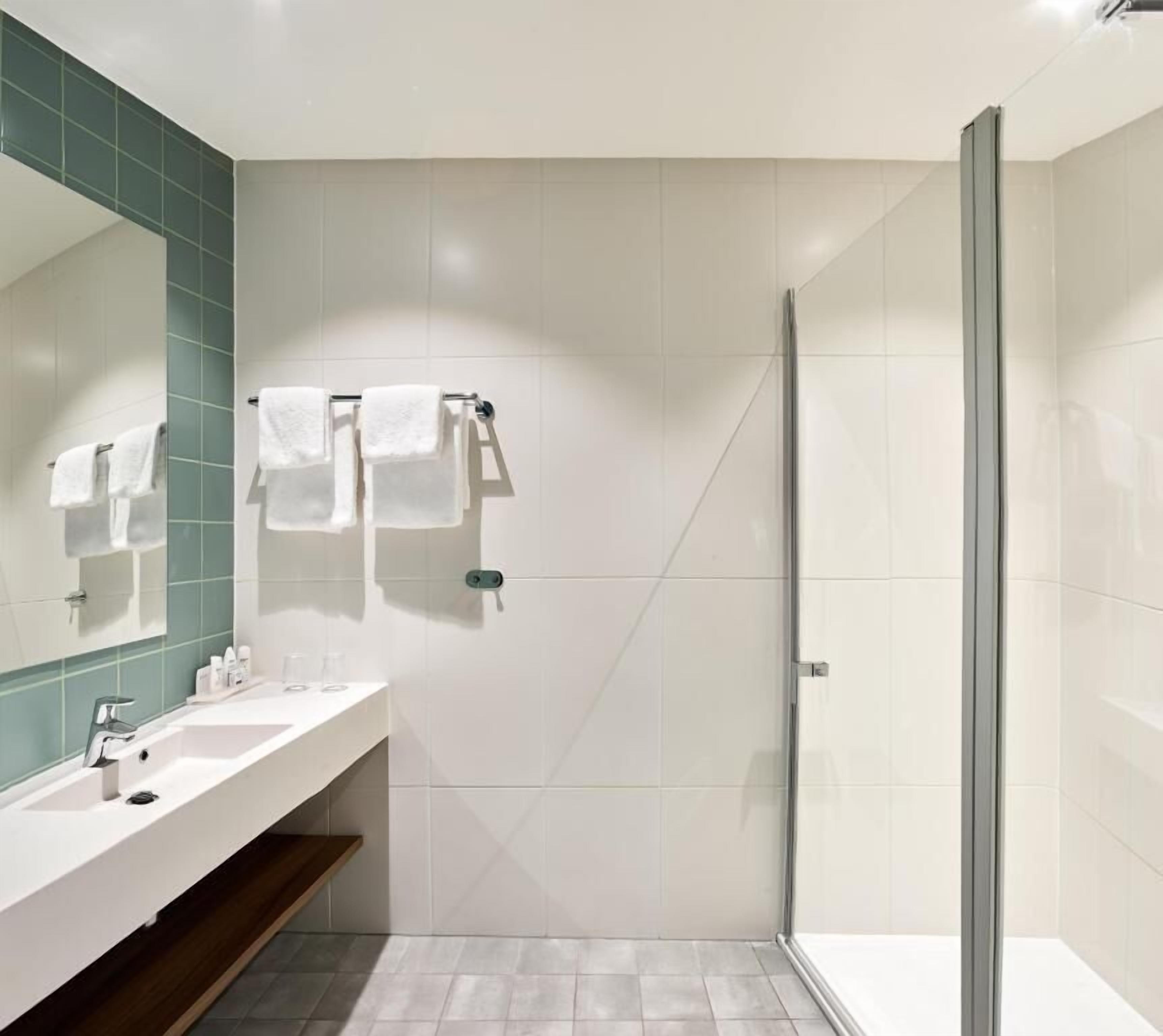 Un baño moderno con cabina de ducha de vidrio, un lavamanos blanco con espejo y una pared de acento con azulejos verdes.