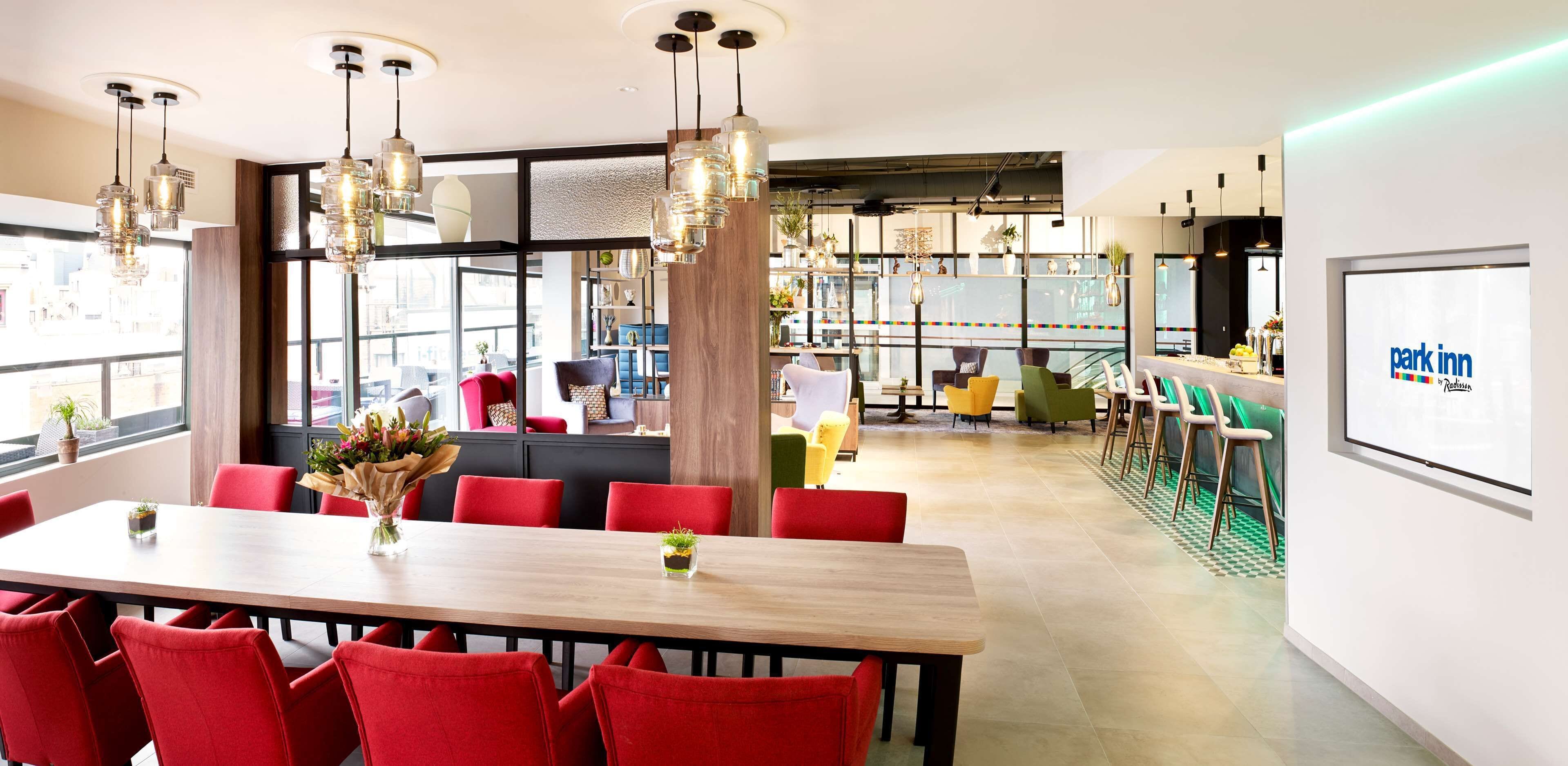 A modern conference room with a large table, red chairs, and hanging pendant lights.