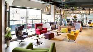 A modern lounge area with comfortable seating, a reception desk, and a view of the city through large windows. - Park Inn by Radisson Hasselt (Hasselt)