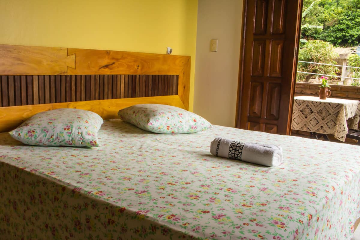 A bed with a floral bedspread, two pillows, and a rolled towel.