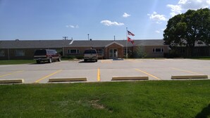A parking lot with two vehicles, a building with a flag, and a grassy area.