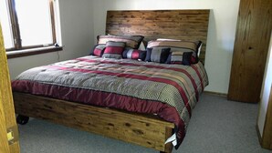 A wooden bed with a geometric patterned bedspread and pillows, a wooden headboard, and a window with blinds.