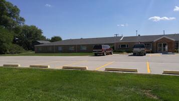 A parking lot with two vehicles, a building with a brick facade, and a grassy area.