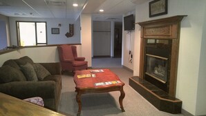 A living room with a sofa, armchair, and a coffee table with magazines. There is a fireplace with a glass door and a television mounted on the wall.