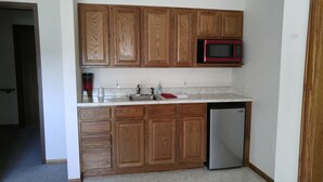 A kitchen with wooden cabinets, a stainless steel refrigerator, a microwave, and a sink.