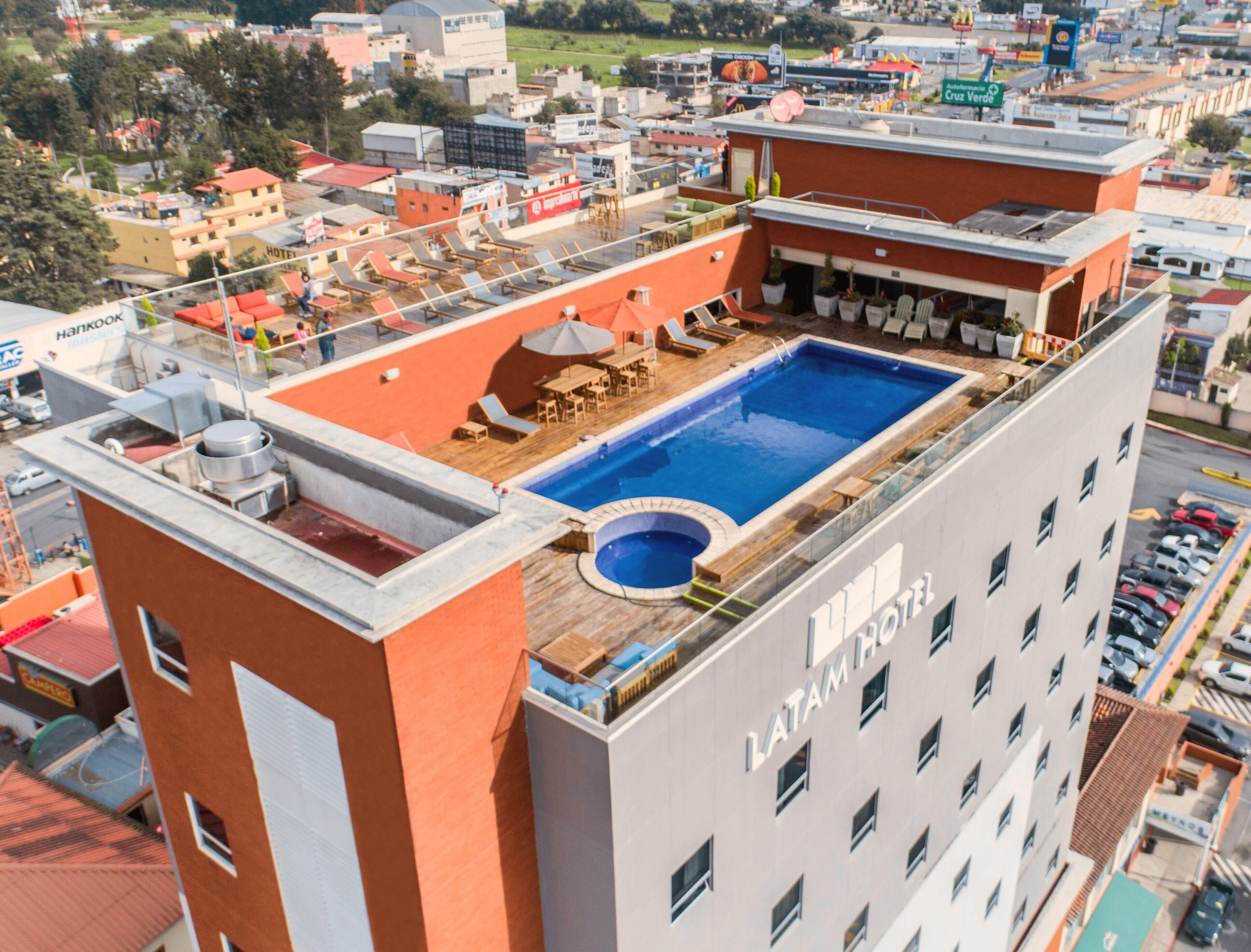 Ein Hotel mit Dachpool, mehreren Balkonen und Blick auf die umliegende Stadtlandschaft.